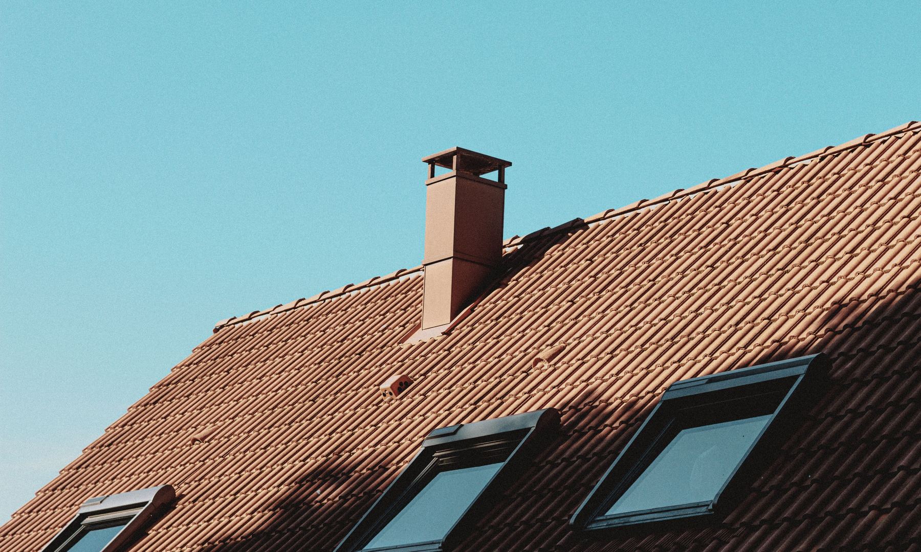 Residential clay-tile roof with a chimney stack and black-framed skylights.